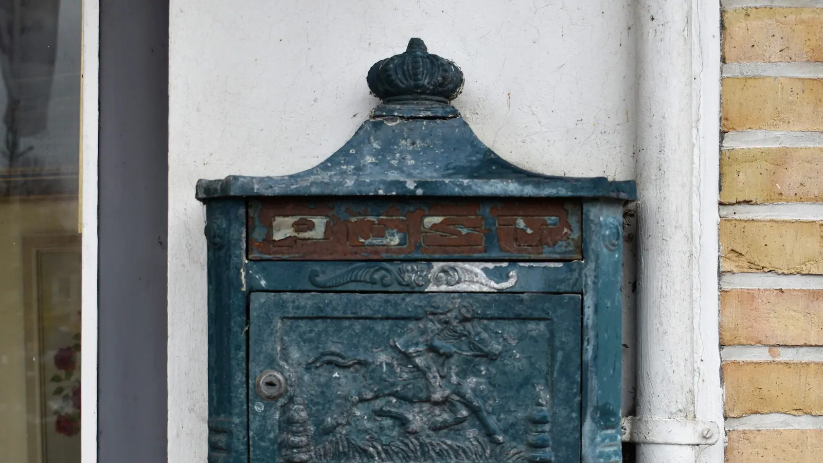 Älterer Briefkasten aus Metall an einer weißen Hauswand
